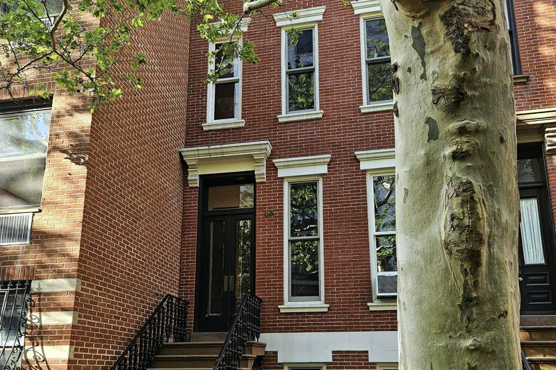 A brick Upper West Side rowhouse and stoop behind a plane tree